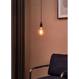 Amber Dimmable LED Globe Bulb E27 G125 lit warm white in a black pendant fitting, hanging against a pink wall beside a curtain and armchair.