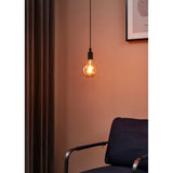 Amber Dimmable LED Globe Bulb E27 G125 lit with visible filament, hanging pendant-style on a black cord against a pink wall in a living room setting.
