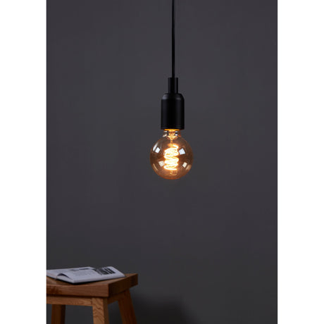 Amber Dimmable LED Globe Bulb E27 G80 4W, lit on a pendant with black cord and fitting, showing its spiral filament, in a room with a wooden stool.