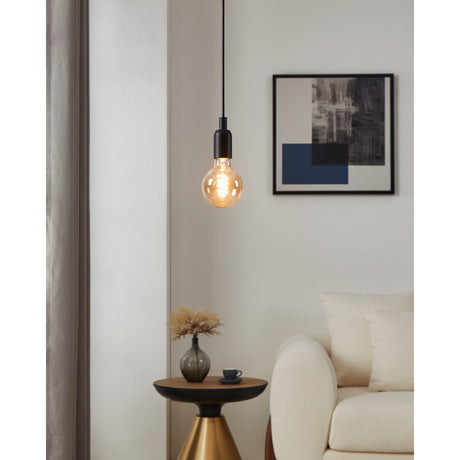 Amber Dimmable LED Globe Bulb E27 G95 glowing in a black pendant fitting above a side table, with a cream sofa and framed art in a living room.