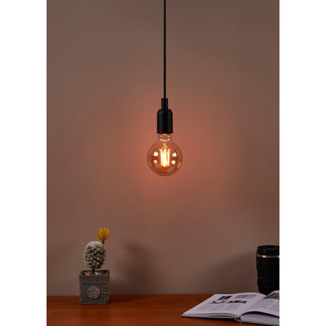 Amber Dimmable LED Globe Bulb E27 G95 lit on a black pendant cord above a desk with a cactus plant, camera lens, and open book nearby.