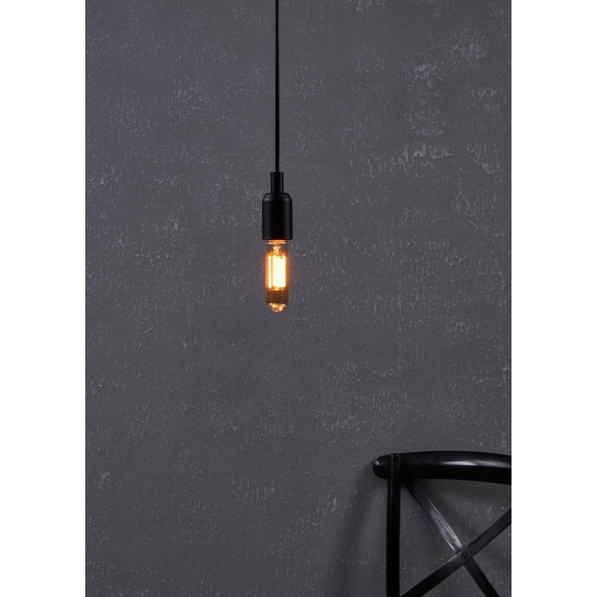 Amber Dimmable LED Tubular Bulb E27 lit warm gold in a black pendant fitting against a dark textured wall, with a black chair visible below.