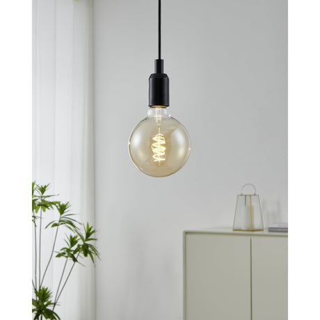 Amber LED globe bulb E27 with spiral filament, G125 glass shade, shown lit in a black pendant fitting against a light living room wall.