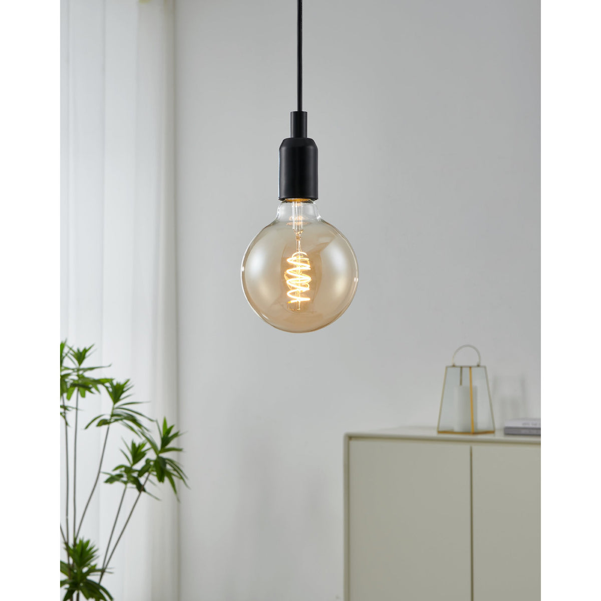 Amber Spiral LED Globe bulb, G125 E27 fitting, glowing warm white, hung from a matte black pendant cord in a neutral living room setting.