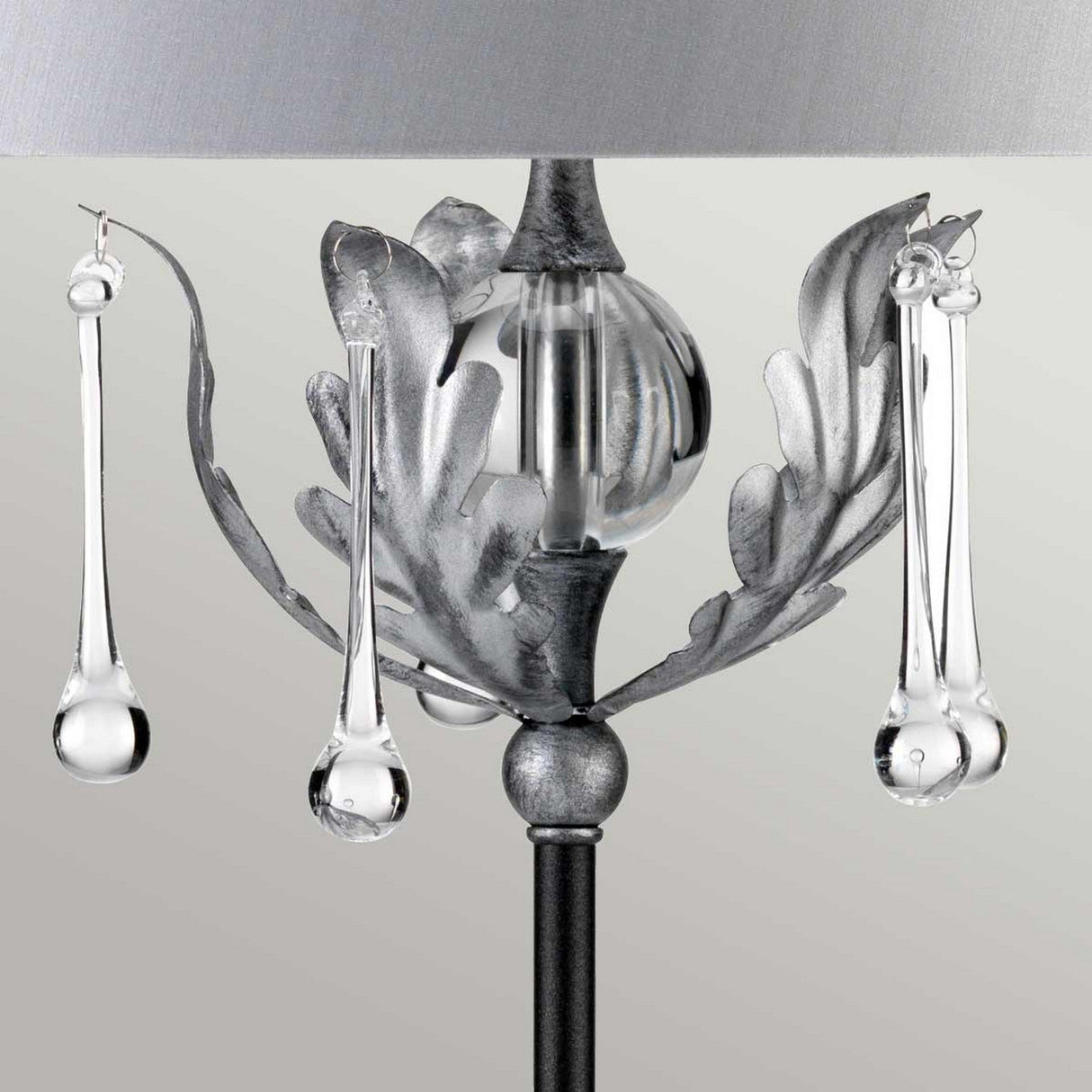 Close-up of the Amarilli 1 Light Table Lamp - Black With Silver Patina, featuring metallic leaf-like accents and suspended glass droplets. This decorative statement piece offers a modern and elegant aesthetic, highlighted by its handcrafted detailing against a neutral background.