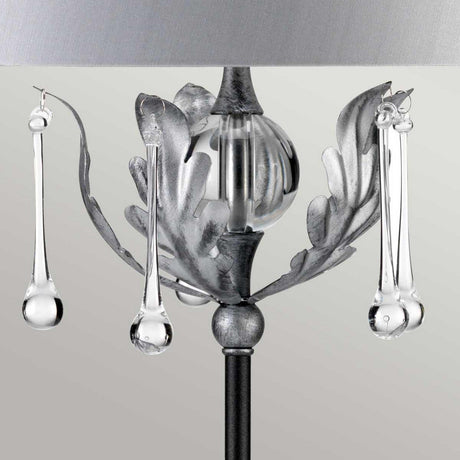 Close-up of the Amarilli 1 Light Table Lamp - Black With Silver Patina, featuring metallic leaf-like accents and suspended glass droplets. This decorative statement piece offers a modern and elegant aesthetic, highlighted by its handcrafted detailing against a neutral background.