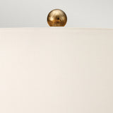A close-up of the Amarilli 1 Light Table Lamp, showcasing its ivory lampshade and decorative gold sphere finial on top, adorned with a bronze base featuring a subtle gold patina finish. The soft gray background enhances the minimalist and elegant ambiance.