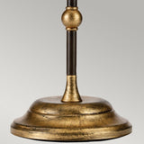 Close-up of the Amarilli 1 Light Table Lamp in bronze with a gold patina finish, featuring a rounded base and a vertical rod with a decorative knob near the top. The ambient light accentuates its craftsmanship against the plain, neutral gray background.