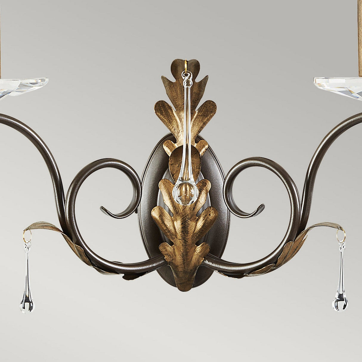 A decorative Amarilli 2 Light Wall Light in a bronze with gold patina finish, featuring ornate scrollwork, leaf designs, and crystal accents, is set against a plain light gray background and echoes the elegance of the Amarilli 5 Light Chandelier.