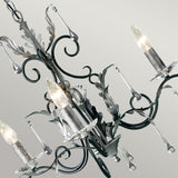 Here's a look at the Amarilli 3 Light Chandelier, expertly handcrafted by Elstead. The piece features detailed metalwork with graceful curves and leaf-inspired motifs, enhanced by a black finish with silver patina. It complements its three candle-like bulbs and dangling crystal ornaments beautifully against a light gray backdrop.