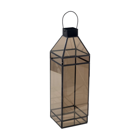 Andranomena Glass Candle Lantern, a tall square lantern with smoked bronze-tinted glass panels in a thin black metal frame, pyramid top and curved carry handle, shown on a plain white background.
