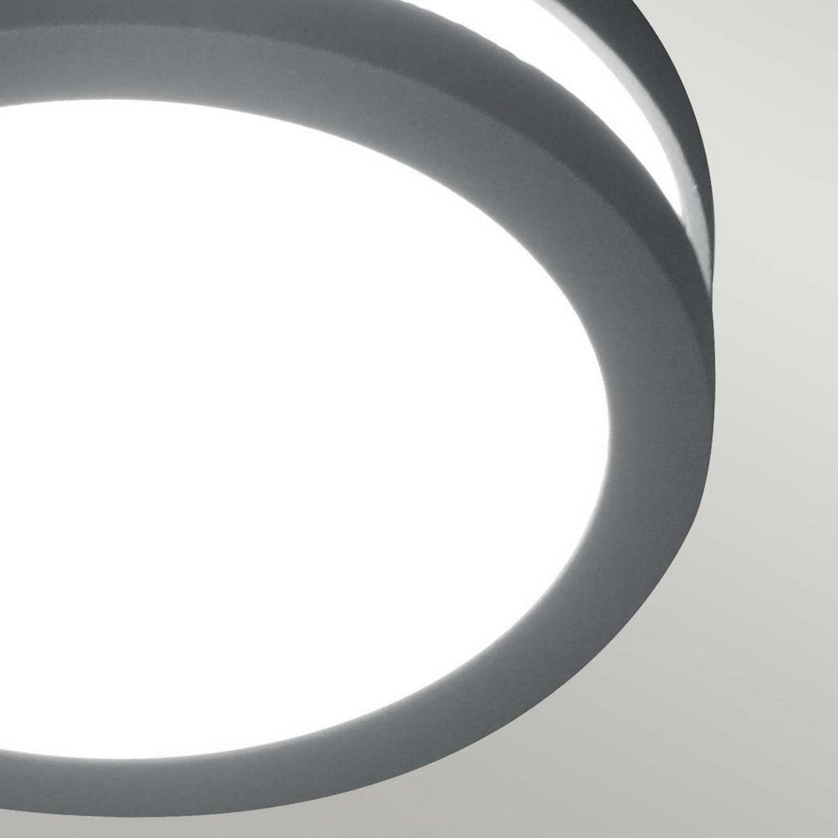 A close-up view of the Ano-1 Outdoor Wall & Ceiling Light in a sleek graphite finish, showcasing its modern design as it emits bright white light against a light gray background.