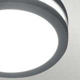 A close-up view of the Ano-1 Outdoor Wall & Ceiling Light in a sleek graphite finish, showcasing its modern design as it emits bright white light against a light gray background.