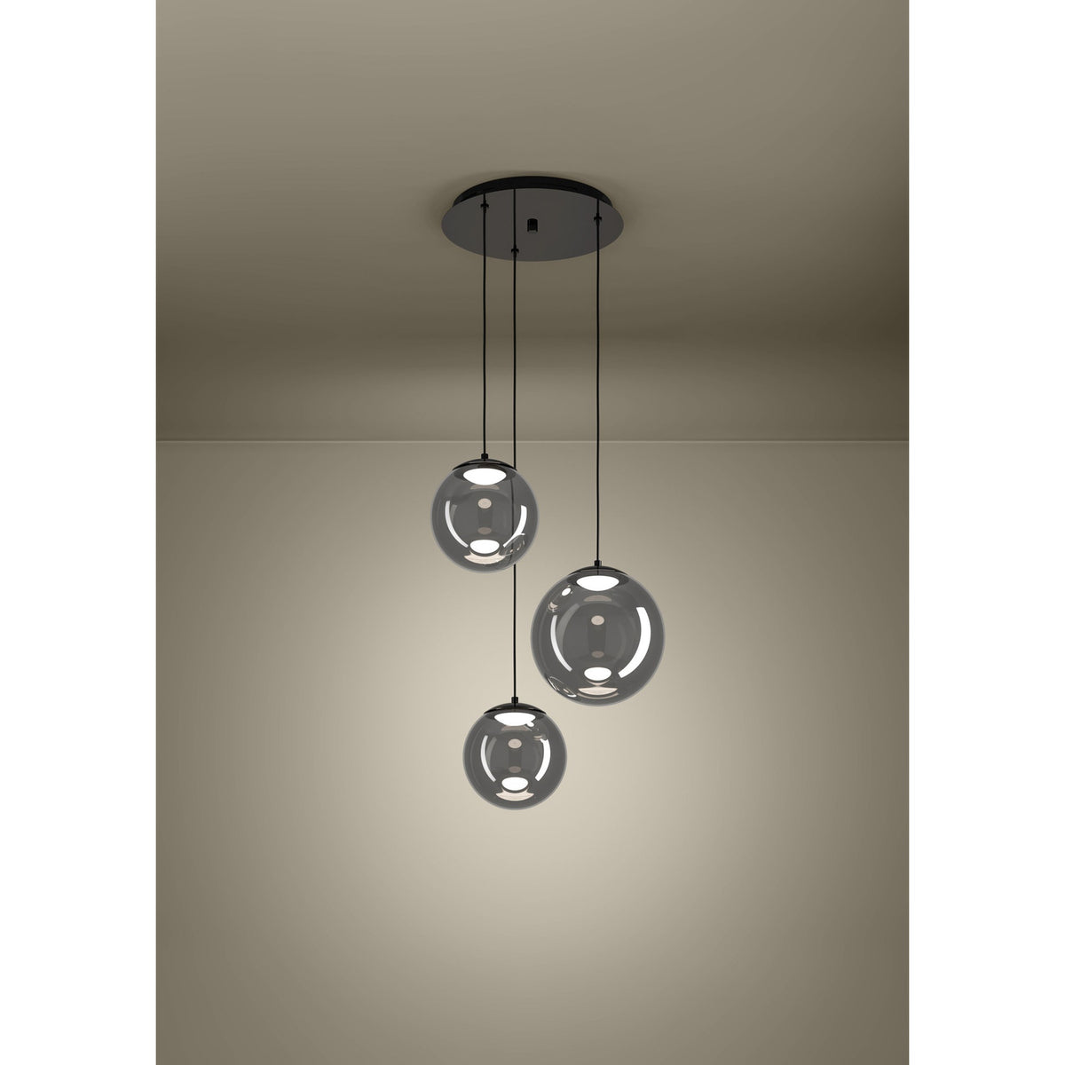 Anorias 3-light pendant with three smoked glass globes of varying sizes on black nickel cords from a round ceiling canopy, shown illuminated in a plain room setting.