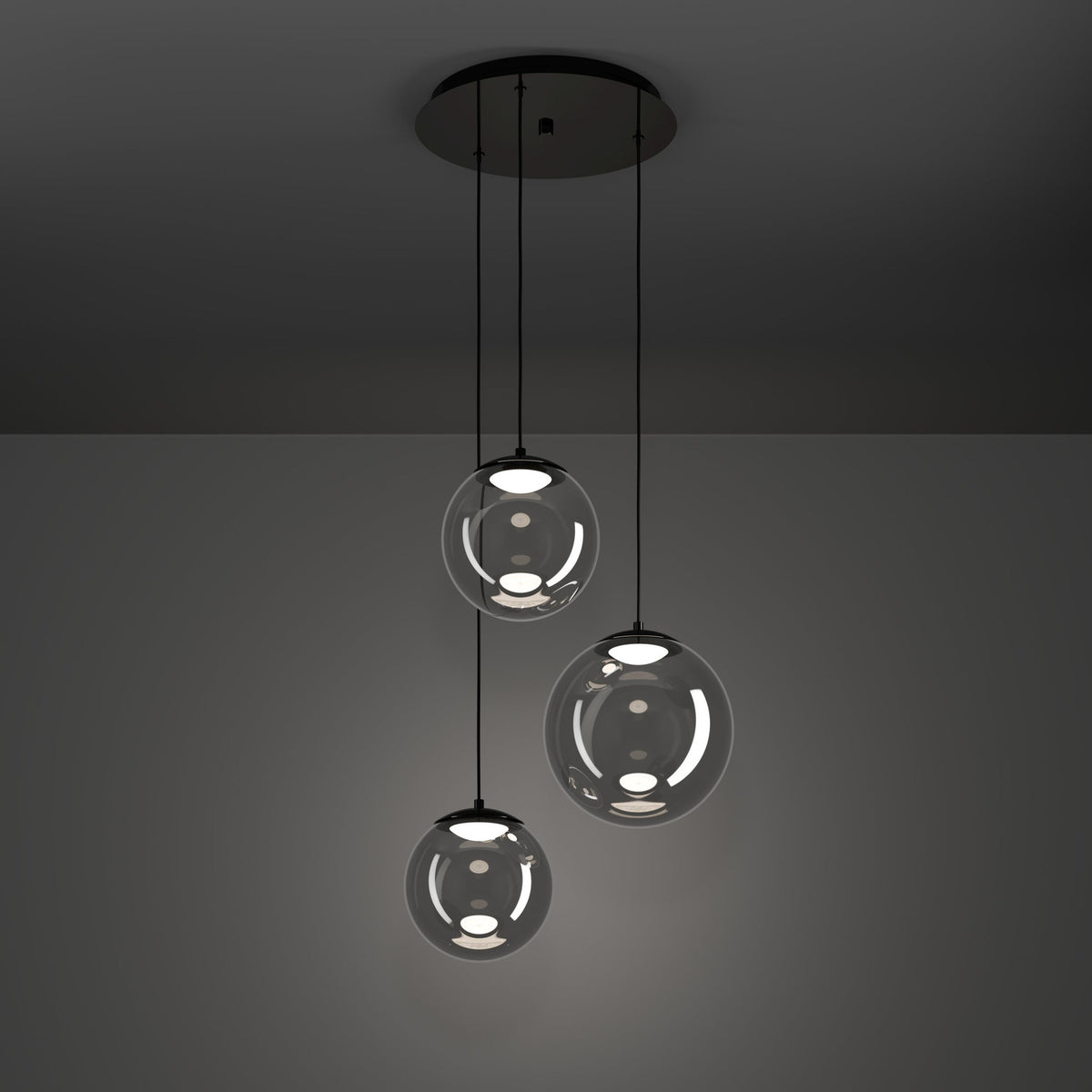 Anorias 3-light pendant with three smoked glass globes of varying sizes on black nickel cords from a round ceiling canopy, shown against a dark grey background.