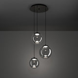 Anorias 3-light pendant with three smoked glass globes of varying sizes on black nickel cords from a round ceiling canopy, shown against a dark grey background.