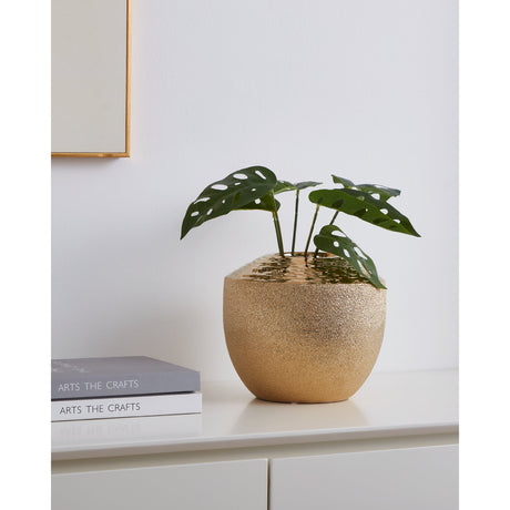 Aramberri Ceramic Vase 17cm in gold, round textured body with a hammered glossy shoulder, holding a leafy plant on a white sideboard beside stacked books.