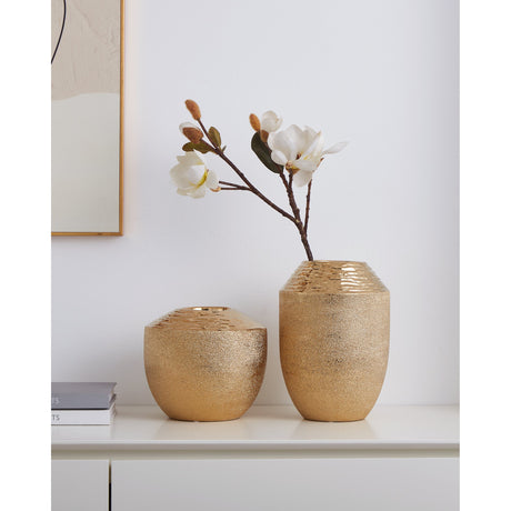 Aramberri Ceramic Vase 25cm in gold with hammered glossy shoulder and sand-textured body, shown with white magnolia stems on a sideboard beside a smaller matching gold vase.