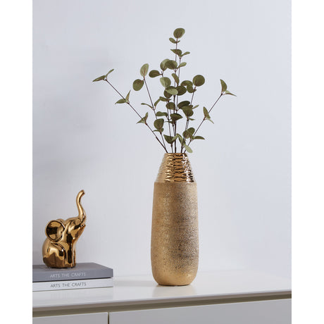 Aramberri Ceramic Vase 35cm in gold with a hammered glossy neck and sandy-textured body, holding eucalyptus stems on a sideboard beside a gold elephant figurine and stacked books.