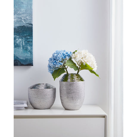 Aramberri ceramic vase in silver with mirror-like rippled shoulder and textured lower body, shown with blue and white hydrangeas beside a smaller matching vase on a white sideboard.