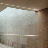 Arcus 2m plaster-in LED profile forming an illuminated recessed line where a stone-tiled wall meets the ceiling in a corridor setting.