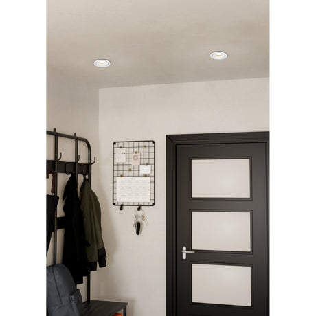 Arenals LED Downlight in white, shown recessed in a hallway ceiling with a slim rim, illuminating a coat rack, wall organiser, and dark panelled door.