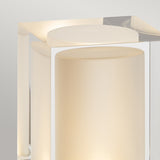 A close-up of the Arendal 1 Light Medium Bollard in Black, featuring a frosted glass cylindrical center encased within a sleek square frame. Emitting a soft, warm glow reminiscent of coastal lighting, it highlights the minimalist design against a neutral background.