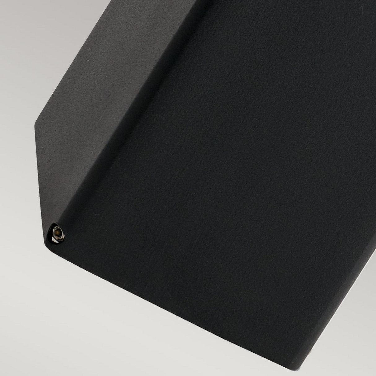 Close-up of an elegant black geometric object, much like the Arendal 1 Light Medium Bollard - Black, displaying a sharp angle and a small screw in one corner, set against a light gray background. Its design reflects chic outdoor lighting styles with coastal lighting influences.