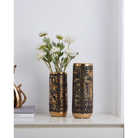 Arroyito Ceramic Vase 25cm in black and gold with textured bubbled finish and polished gold rim, shown with white flowers on a shelf beside books.