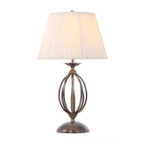 The Artisan Table Lamp - Aged Brass boasts an ornate spherical base design and is complemented by a pleated white shade, producing a warm glow when illuminated.