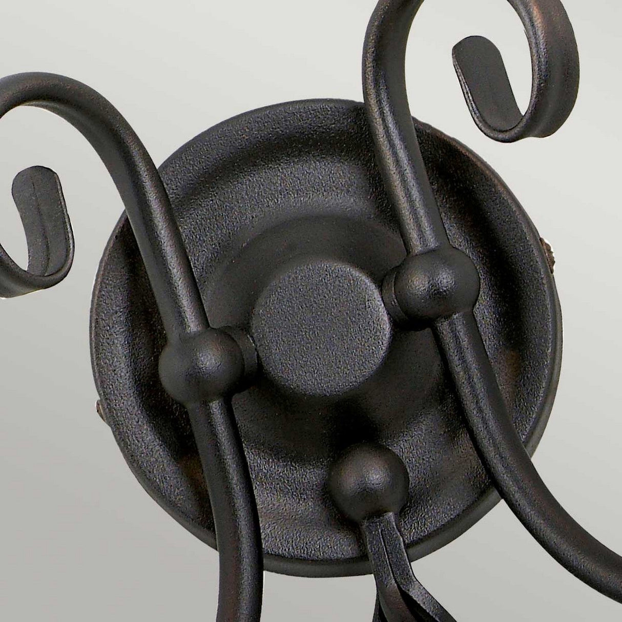 A detailed view of the Artisan 2 Light Wall Light - Black, highlighting its handcrafted metal scrolls. This decorative piece features curved arms that extend from a circular base, adorned with elegant scroll-like designs.