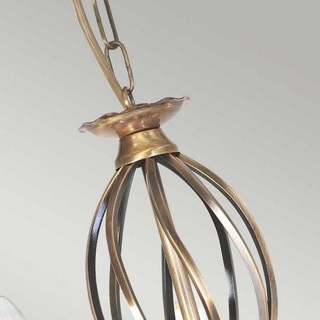 Close-up of the Artisan 5 Light Chandelier in aged brass, featuring a twisted metal design that serves as an ornate decorative focal point. The chandelier is suspended by a chain against a neutral gray background.