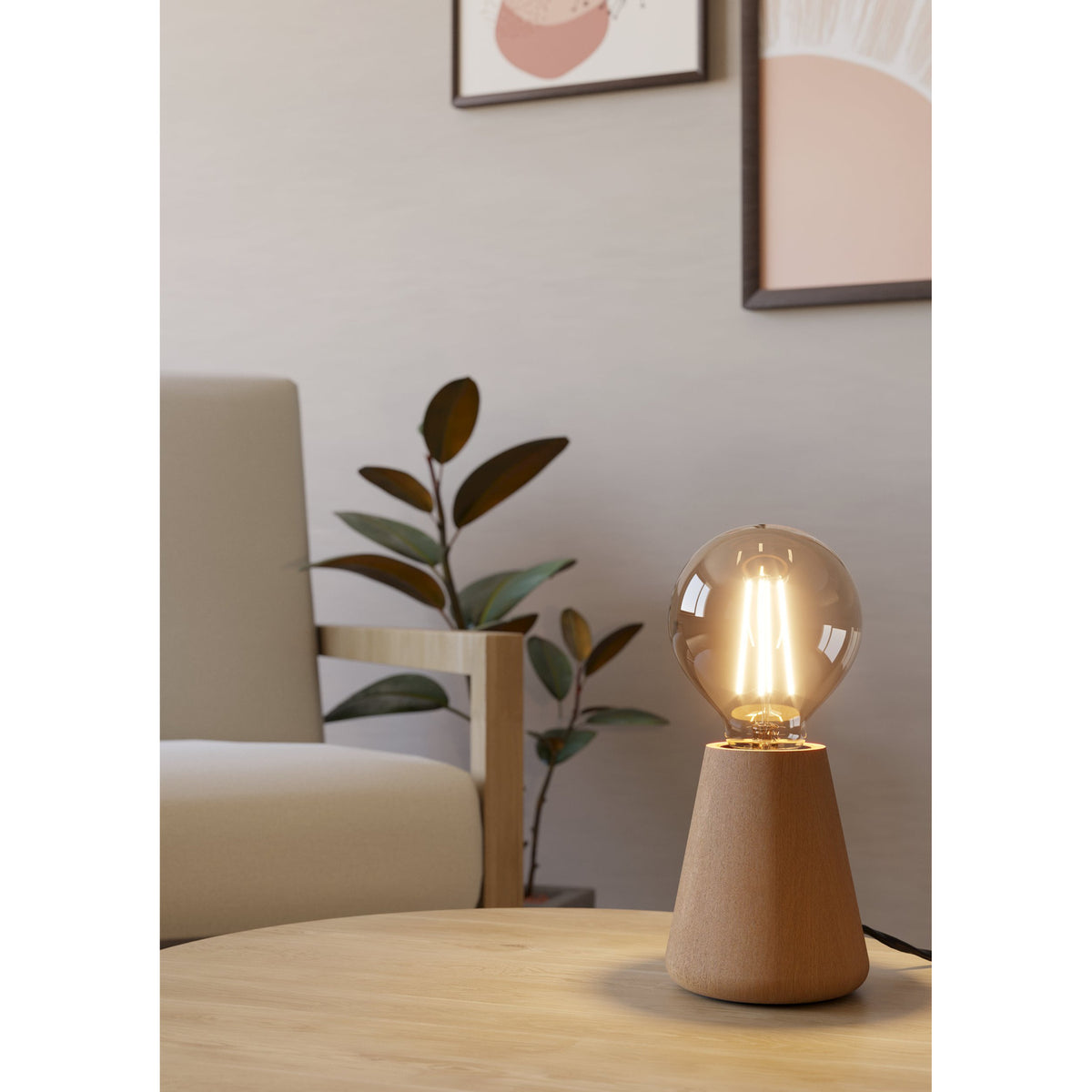 Asby Table Lamp in light wood with tapered base and exposed E27 bulb, shown lit on a wooden coffee table in a living room setting.