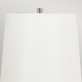 Close-up view of a sleek white lampshade, which is part of the Ascent Table Lamp - Black/White with its contemporary design. The metallic lamp post rises elegantly above the lampshade's surface. The light gray background enhances its black and white aesthetic, offering a stylishly neutral setting.