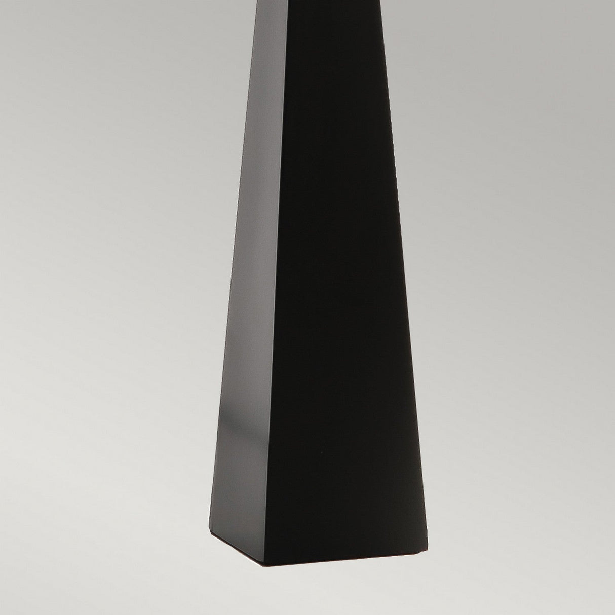 A tall, sleek black obelisk stands against a gradient gray background, highlighting its smooth and glossy finish—a testament to contemporary design reminiscent of the Ascent Table Lamp - Black/White.