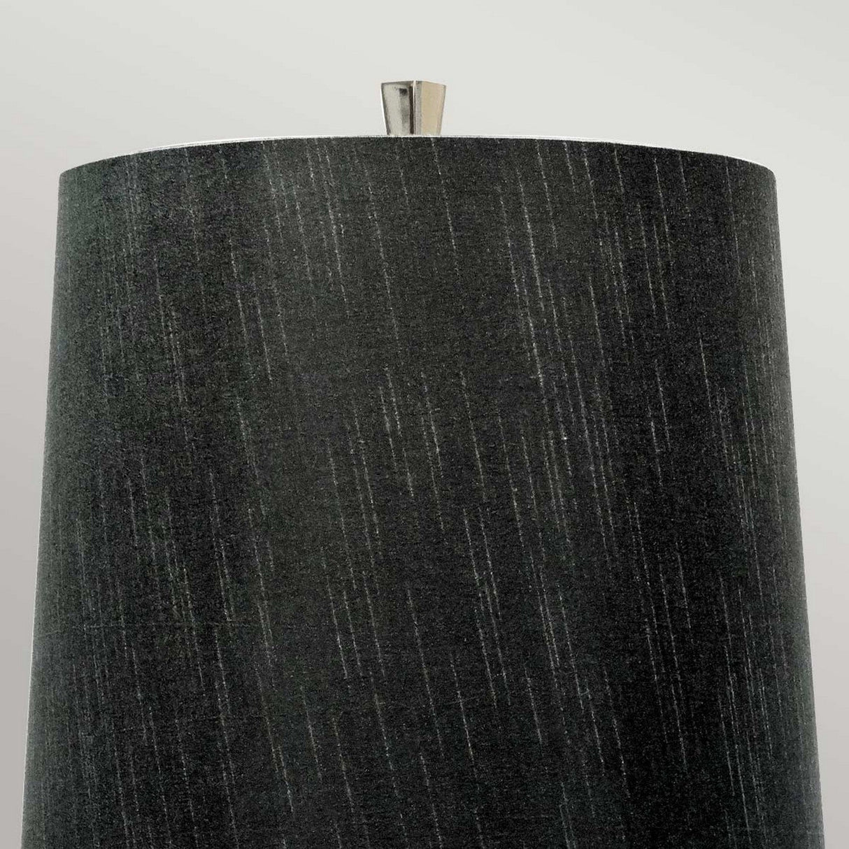 A close-up of the Ascent Table Lamp With Black Shade - Polished Nickel showcases its tall, cylindrical black shade adorned with subtle vertical lines and a small metallic finial in a polished nickel finish, set against a light gray background.