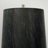 A close-up of the Ascent Table Lamp With Black Shade - Polished Nickel showcases its tall, cylindrical black shade adorned with subtle vertical lines and a small metallic finial in a polished nickel finish, set against a light gray background.