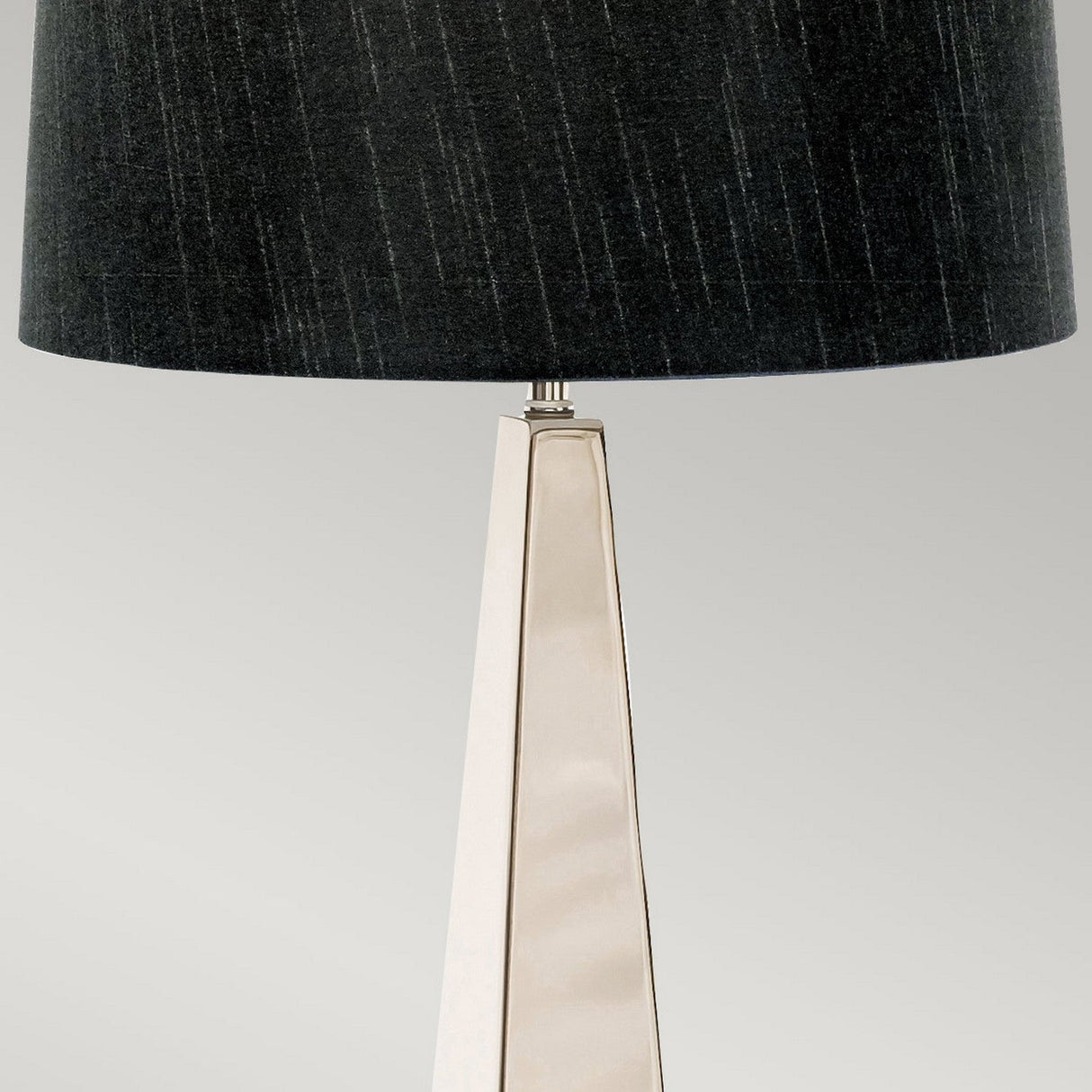 Presenting the Ascent Table Lamp with Black Shade - Polished Nickel, which boasts a polished nickel finish and a modern, triangular metallic base. Its textured black shade adds a touch of contemporary style, beautifully enhancing any neutral gray setting.