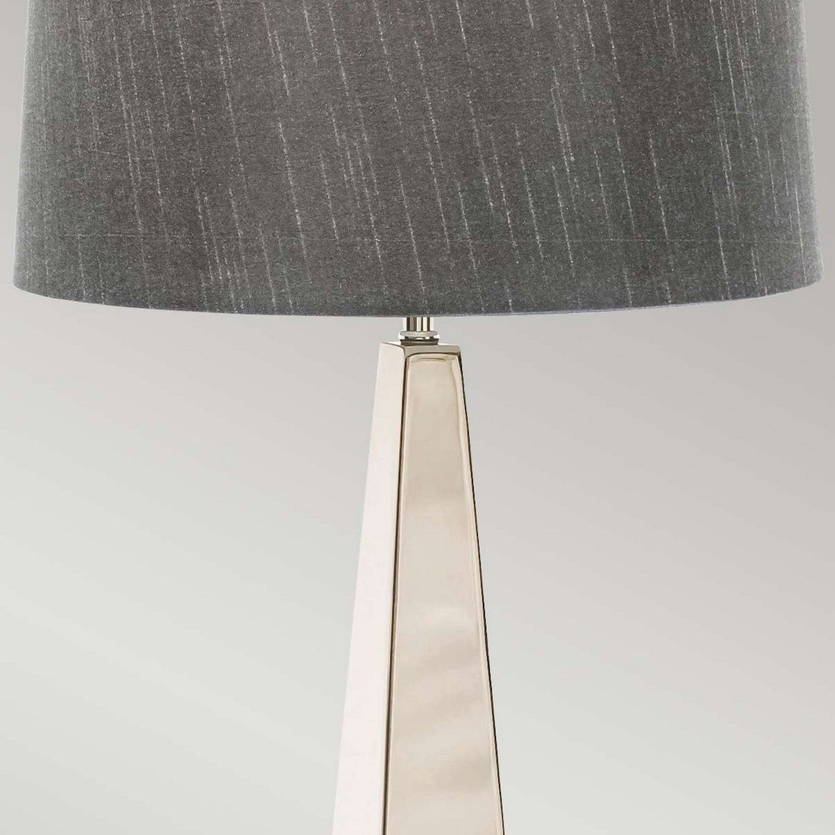 The Ascent Table Lamp With Dark Grey Shade - Polished Nickel showcases a tall, triangular metallic base with a polished nickel finish and is complemented by a large, dark gray fabric lampshade. It stands out against a light gray background, offering a minimalist and elegant look.