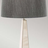 The Ascent Table Lamp With Dark Grey Shade - Polished Nickel showcases a tall, triangular metallic base with a polished nickel finish and is complemented by a large, dark gray fabric lampshade. It stands out against a light gray background, offering a minimalist and elegant look.