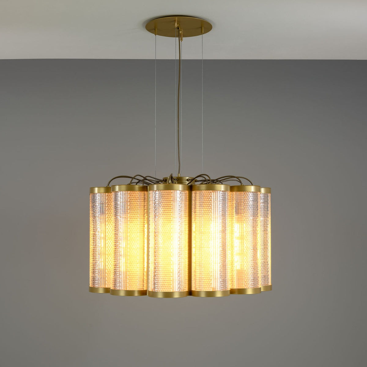 Ashford Acrylic 20 Light Chandelier with scalloped circle of ribbed clear acrylic cylinders and brass trim, suspended from a round brass ceiling plate on a grey background.
