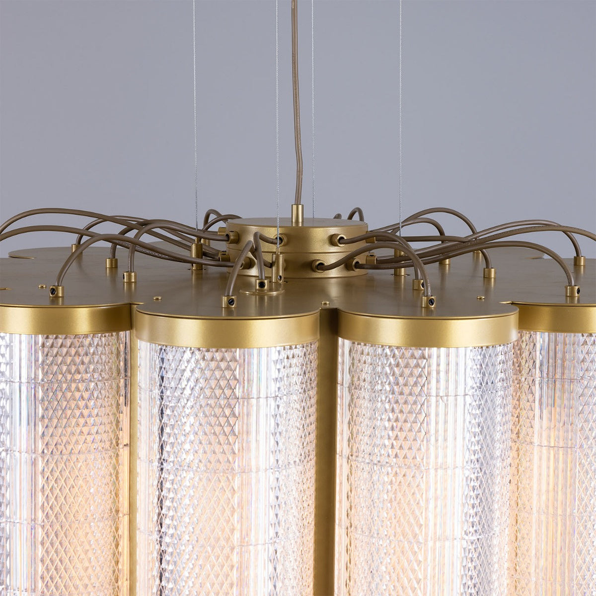 Close-up of the Ashford Acrylic 20 Light Chandelier showing scalloped clear ribbed cylinders with gold-toned metal rims and exposed wiring at the canopy, against a plain grey background.