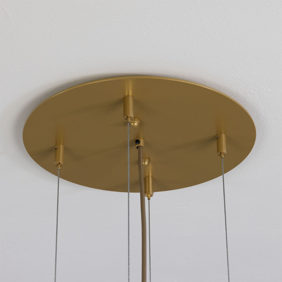 Oval gold ceiling canopy for the Ashford chandelier, showing multiple cable suspension points and a fabric-wrapped cord against a plain white ceiling.