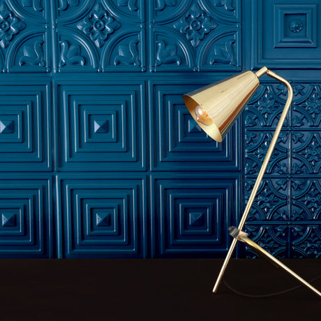 Astana Brass Table Lamp with cone shade on an angled stem and tripod base, shown against a dark blue patterned panel wall.