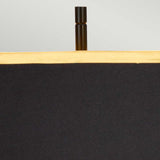 A close-up of the Atlas Table Lamp in brushed brass showcases its black lampshade with a gold rim, elegantly perched on a thin vertical metal post and resting on a marble base. The plain light gray background enhances its minimalist and modern design.