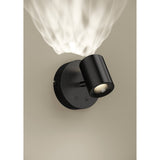 Auro LED Ceiling Light in black, round steel backplate with an angled cylindrical head, mounted on a neutral wall with a warm light beam visible above.