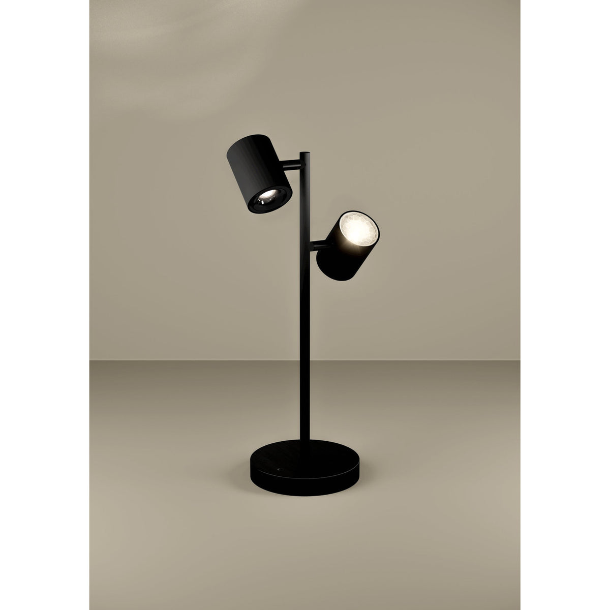 Auro LED Table Lamp in black steel with two adjustable cylindrical spot heads on a slim stem and round disc base, set against a plain neutral background.