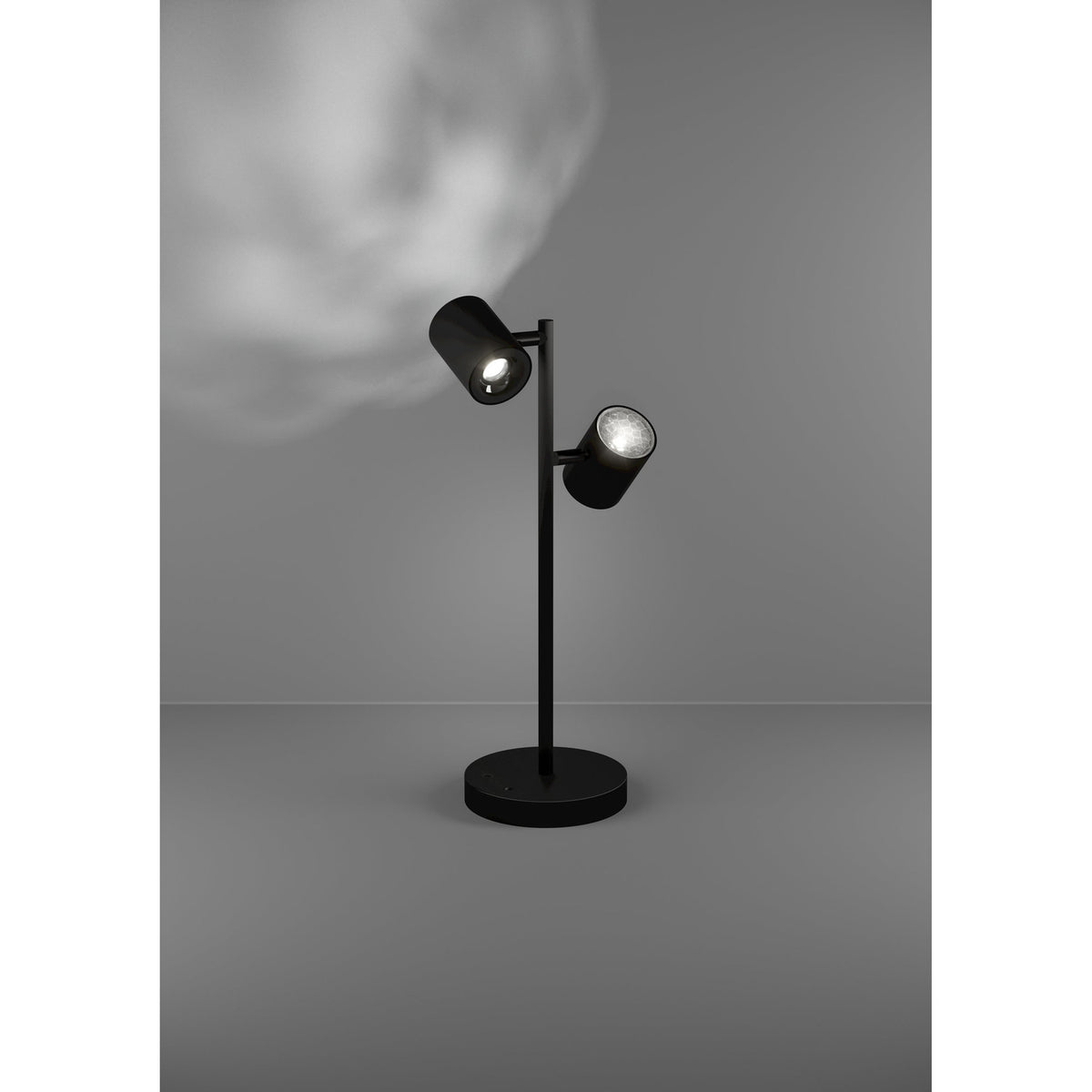 Auro LED Table Lamp in black steel with two adjustable cylindrical spot heads on a slim stem and round disc base, shown lit against a grey background.