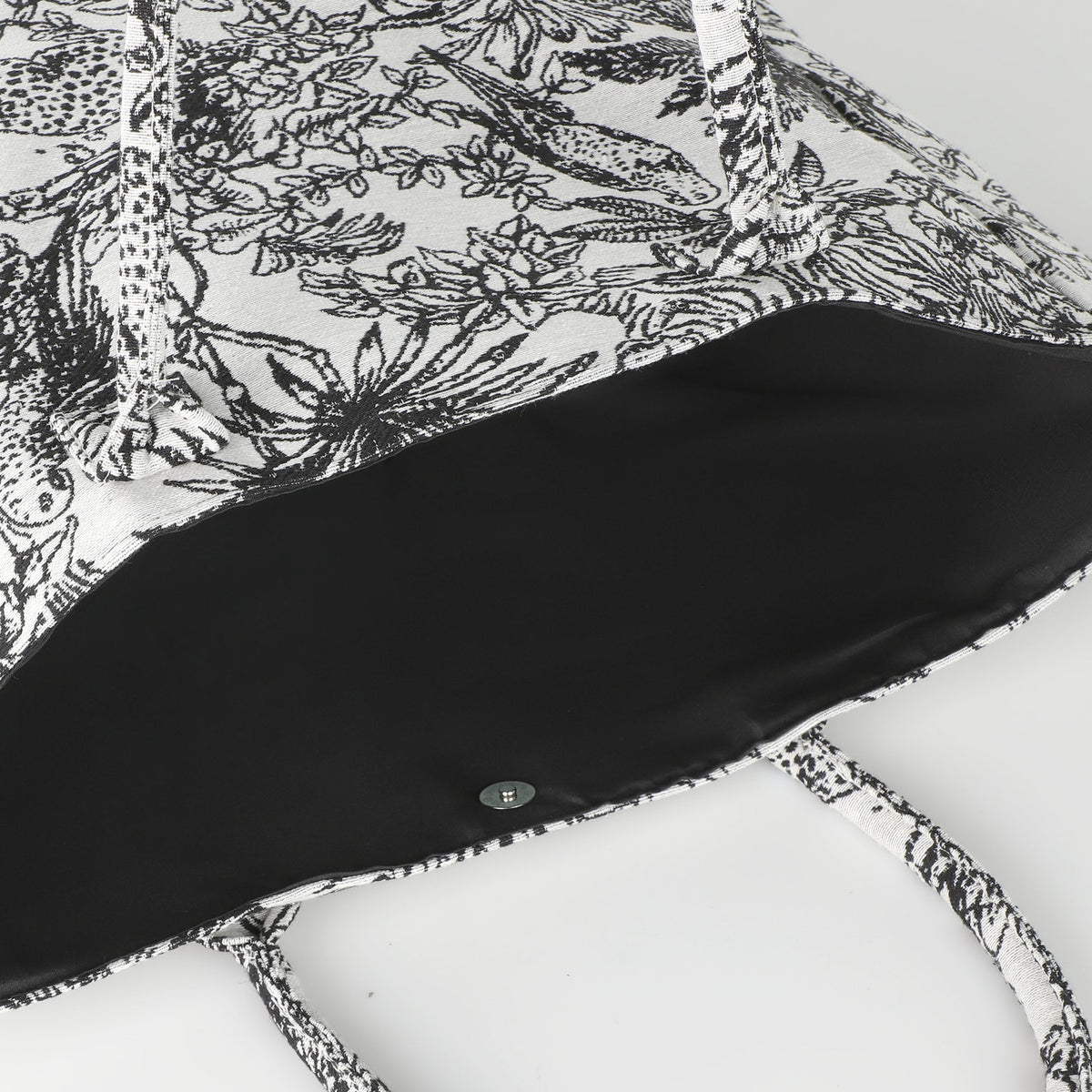 Bachuma Bag in Black showing the open top with plain black interior lining, press-stud closure, and black-and-white jungle toile print fabric and handles.
