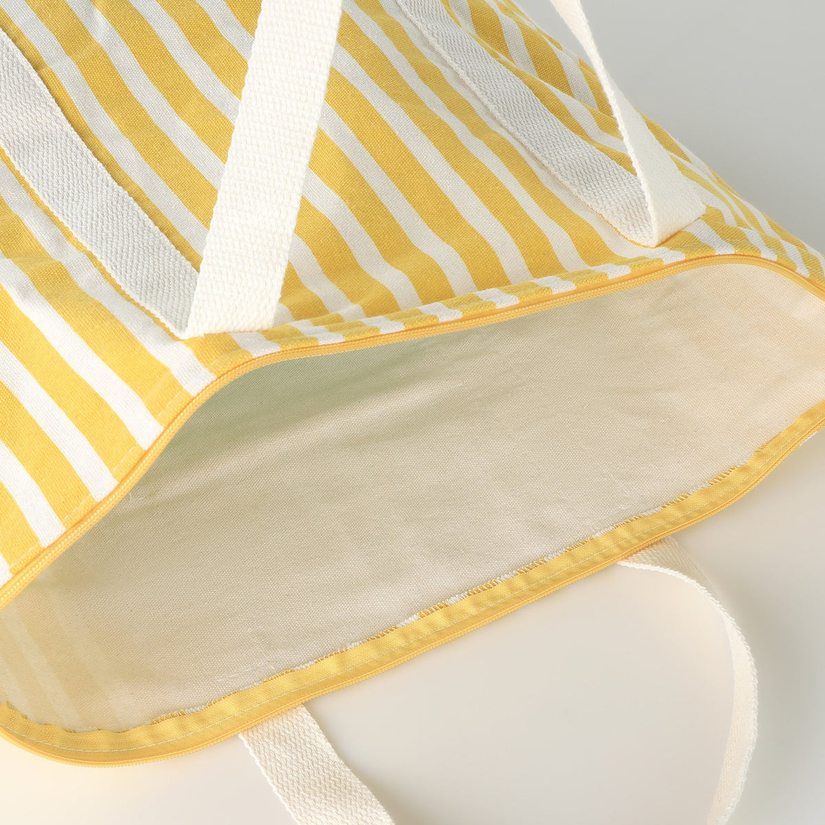 Close-up of the Bachuma Bag, a yellow and white striped fabric tote, showing the cream interior lining, zip trim, and webbing handles.
